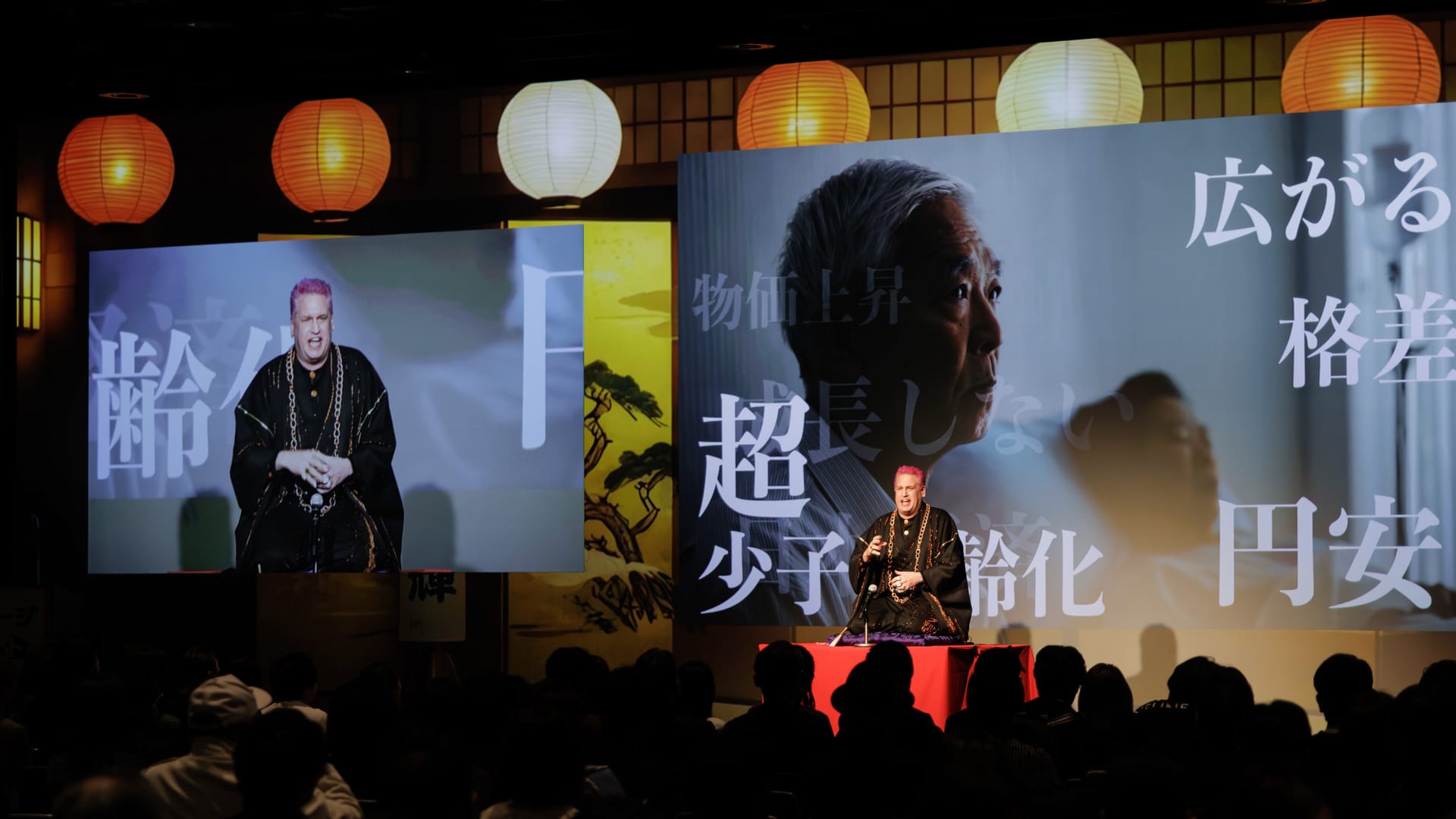 「超少子高齢化」「物価上昇」「広がる格差」を映すスクリーンと客席