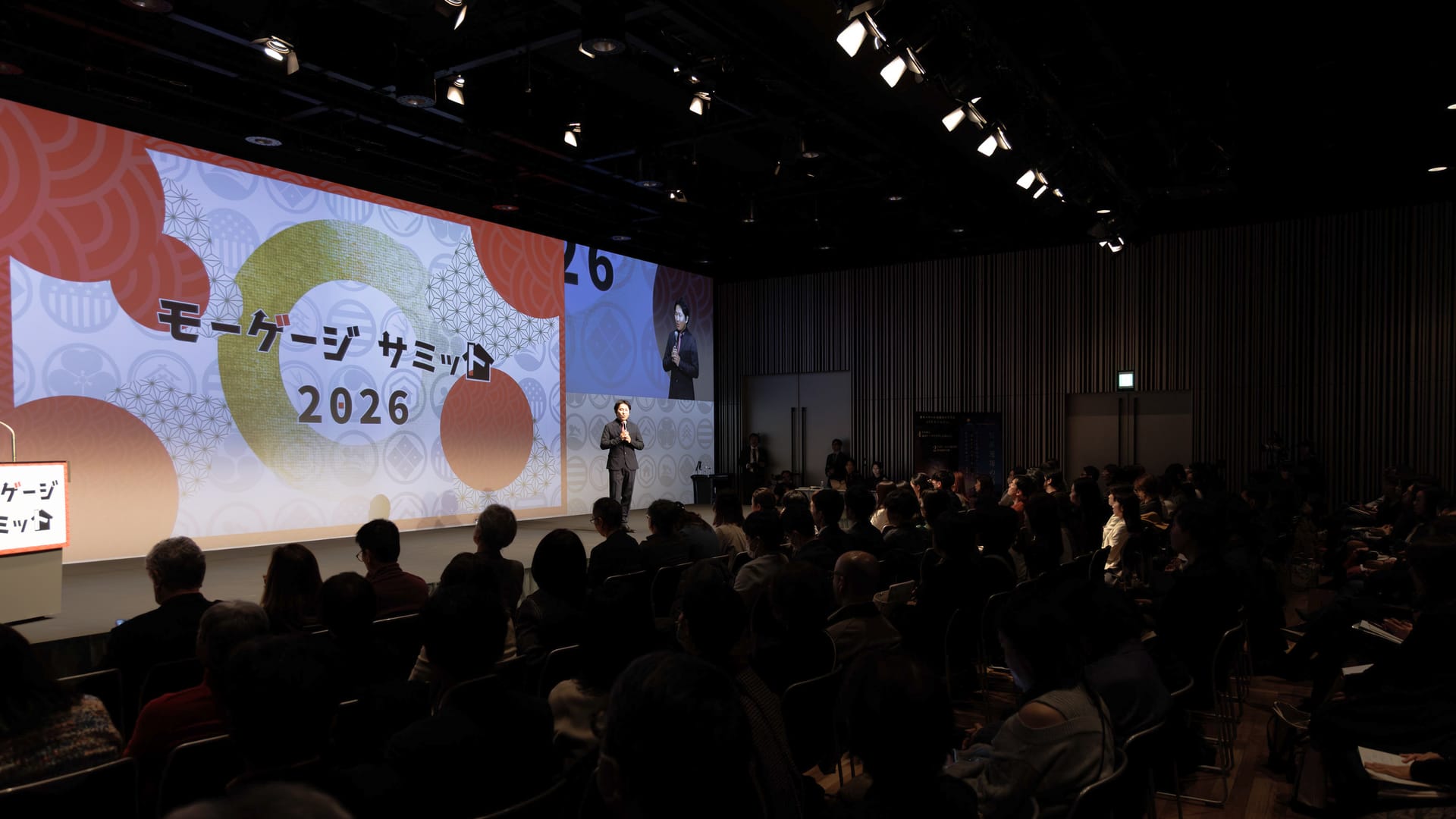 モーゲージサミット2026のスクリーンを背に講演する登壇者